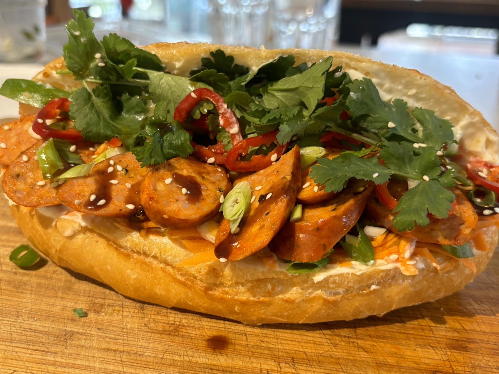 An open bánh mì on a wooden board, topped with chilli, coriander and sesame