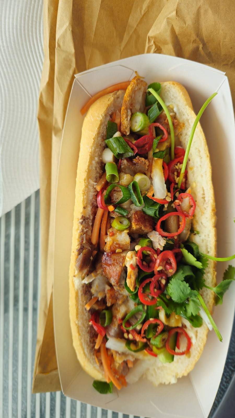 A loaded pork bánh mì with chilli, shallots and coriander in a paper tray