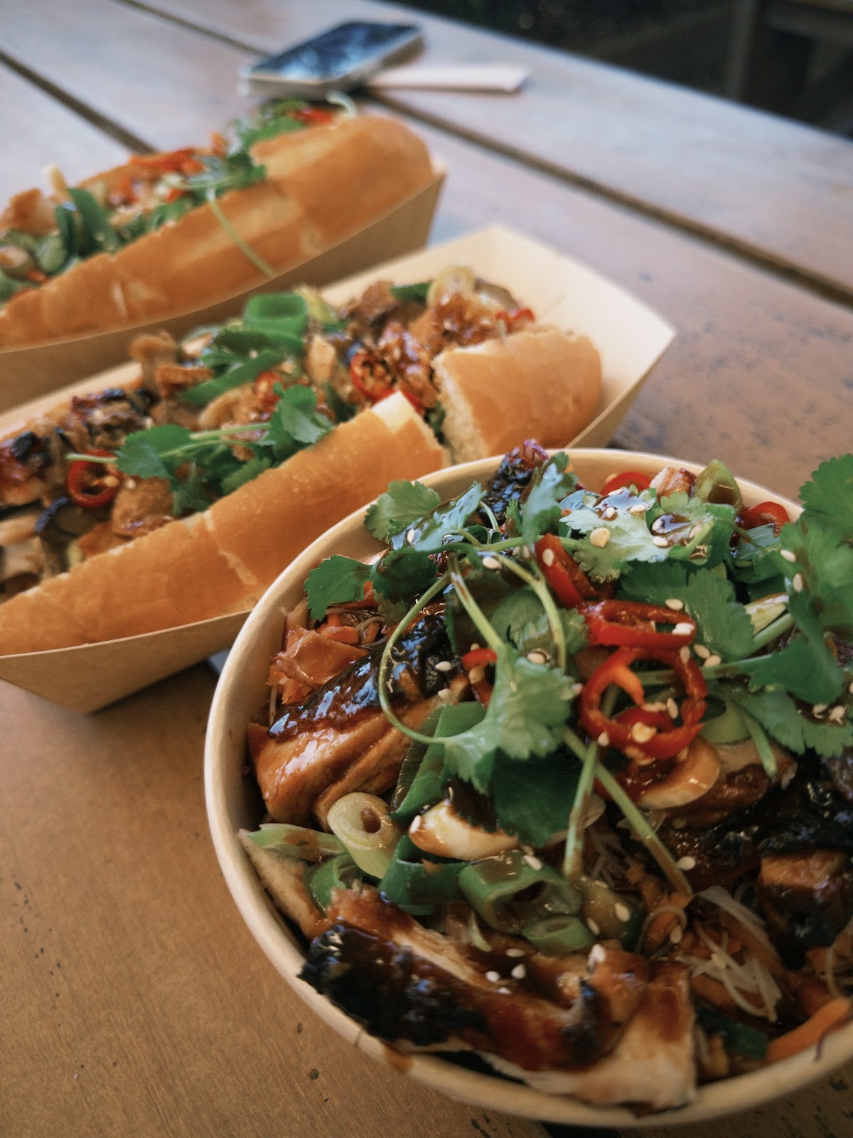 Two bánh mì and a salad bowl on an outdoor timber table